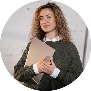 Smiling woman with curly hair holding a closed laptop.