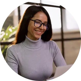 Smiling woman wearing glasses and a light gray turtleneck working at a desk.